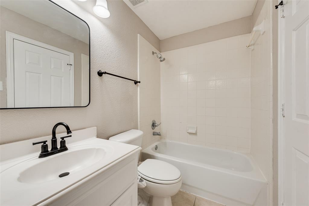 Bathroom featuring a vanity with a white countertop and oval sink, matte black widespread faucet, rectangular mirror with black frame, and a shower-tub combination with white tile surround