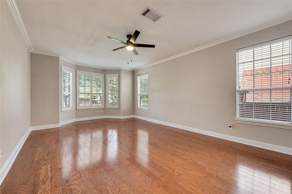 Spacious room featuring wood-finish flooring, crown molding, multiple windows with plantation shutters, and a ceiling fan