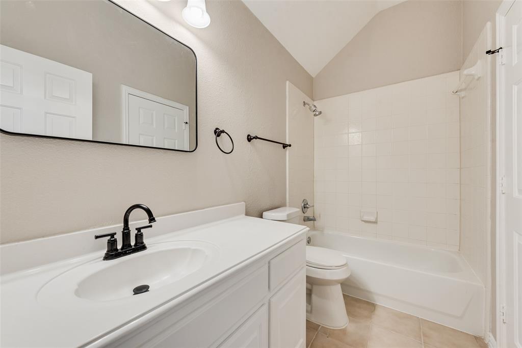 Bathroom featuring a vaulted ceiling, vanity with a white countertop and oval undermount sink, matte black faucet, and a shower-tub combination with tile surround