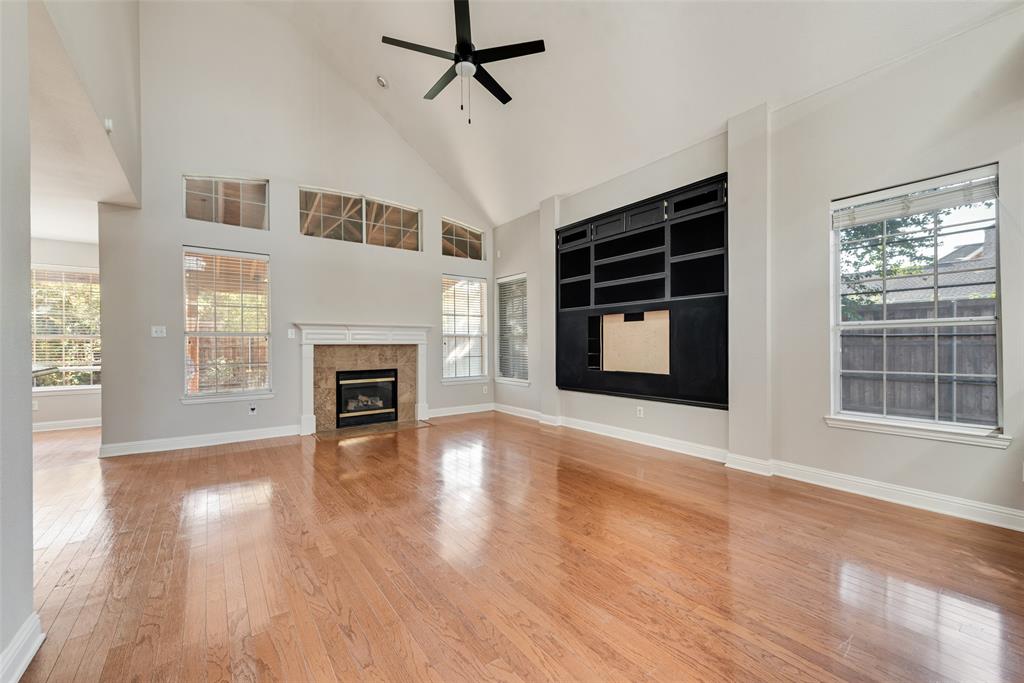 Vaulted ceiling living area featuring wood-finish flooring, a fireplace with a stone-surround mantel, built-in black cabinetry, and oversized windows with transom accents