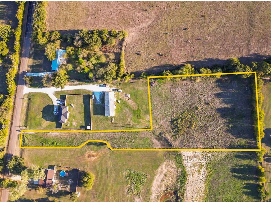 Aerial perspective of acreage featuring open grass pasture, boundary perimeter markers, and mature tree lines