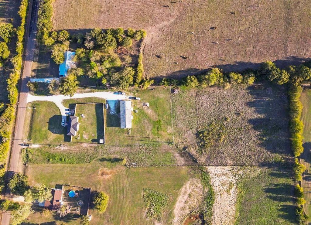 Aerial perspective of expansive acreage featuring mature trees, a gravel driveway, fenced perimeter, and open grassy terrain