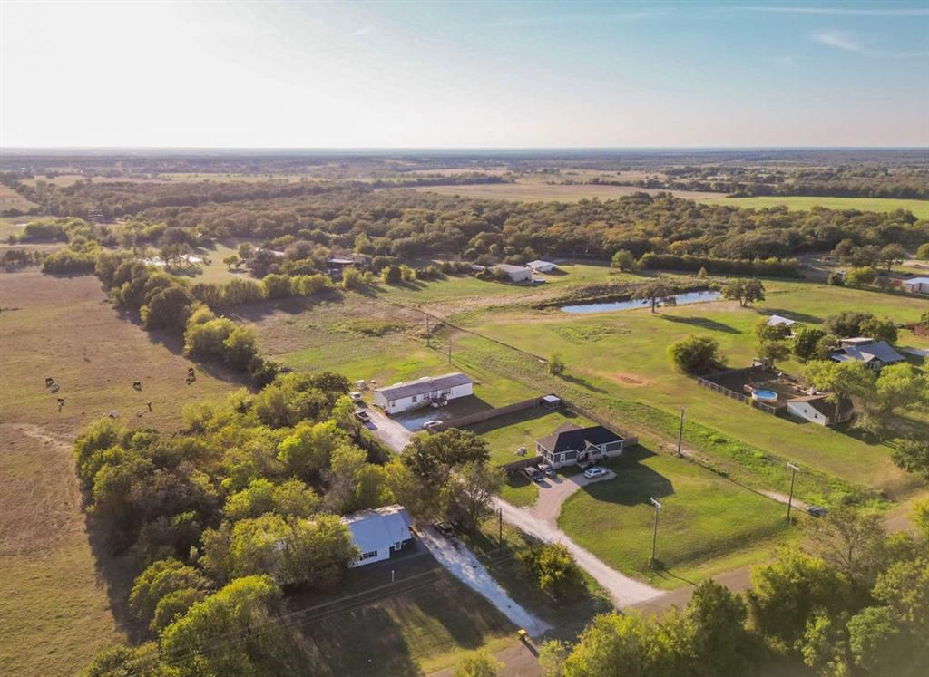 Aerial perspective of a sprawling property featuring expansive acreage, mature tree clusters, open pasture land, and a private pond