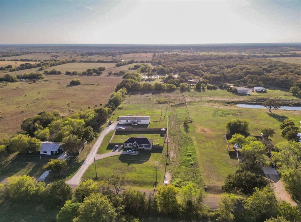 Aerial view of expansive acreage featuring multiple structures, fenced perimeter sections, gravel driveways, and mature tree clusters