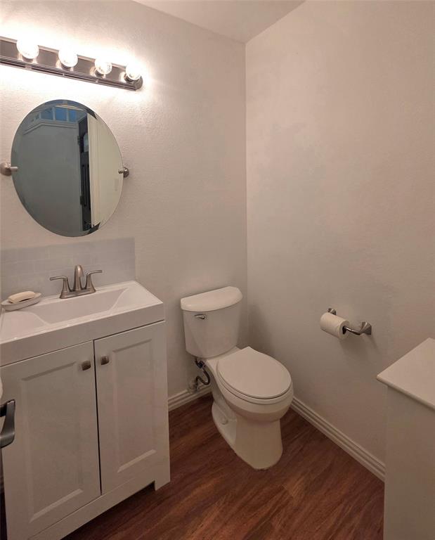 White vanity with a rectangular basin, oval wall-mounted mirror, four-light vanity fixture, wood-finish flooring, and subway tile backsplash