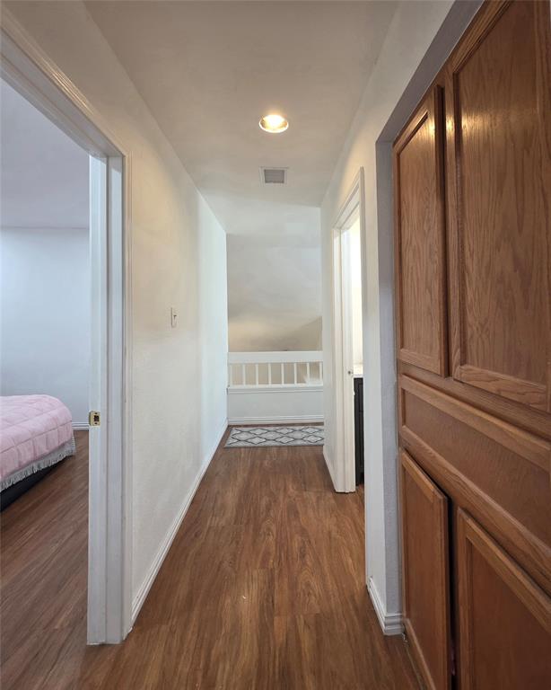 Hallway featuring wood-finish flooring, built-in wooden cabinetry, and a wooden banister