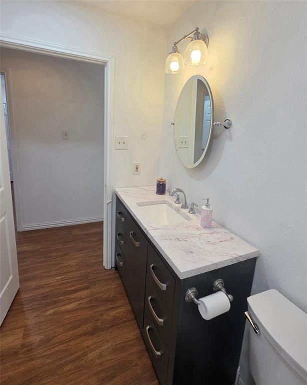 Dark-toned vanity with multi-drawer storage, integrated sink, light-colored patterned countertop, oval wall-mounted mirror, and dual-globe light fixture