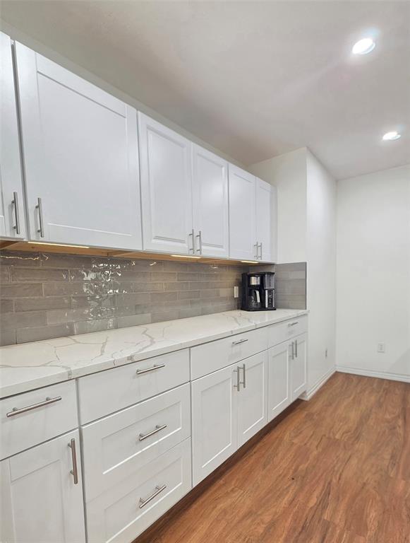 White shaker-style cabinetry, quartz countertops, gray subway tile backsplash, under-cabinet lighting, and wood-finish flooring