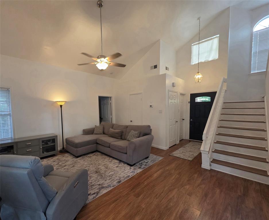Vaulted ceiling featuring a central hanging ceiling fan, wood-finish flooring, staircase with wood-tread steps, and a decorative transom window above the front entrance