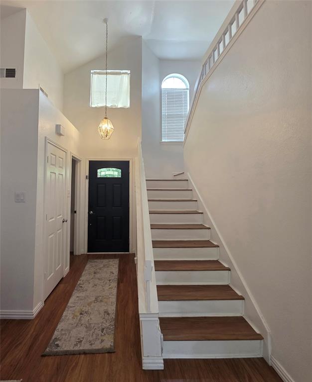 Entryway featuring high ceilings, wood-finish flooring, a pendant light fixture, a staircase with wood-finish treads and white risers, and an arched window