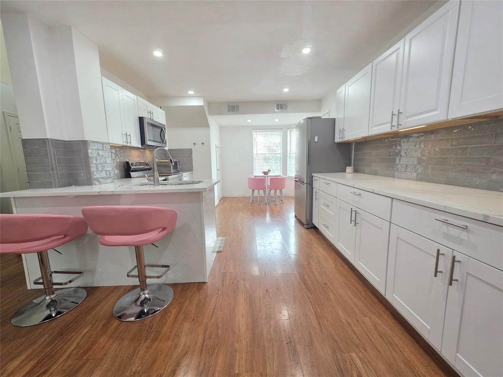 Kitchen featuring white shaker-style cabinetry, solid-quartz countertops, grey subway tile backsplash, stainless steel appliances, and wood-finish flooring