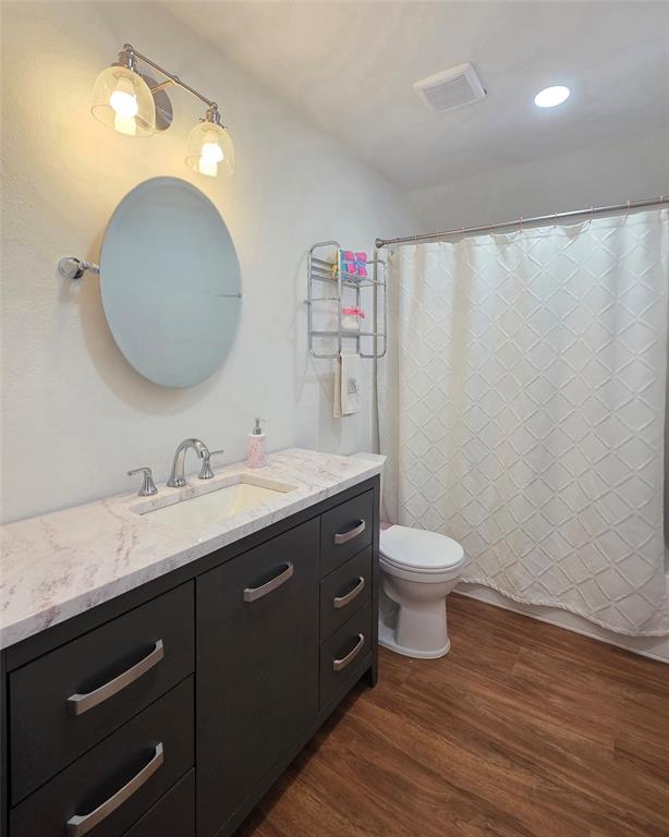 Dark charcoal vanity with a stone-finish countertop, integrated sink, polished metal hardware, circular wall mirror, and wood-finish flooring
