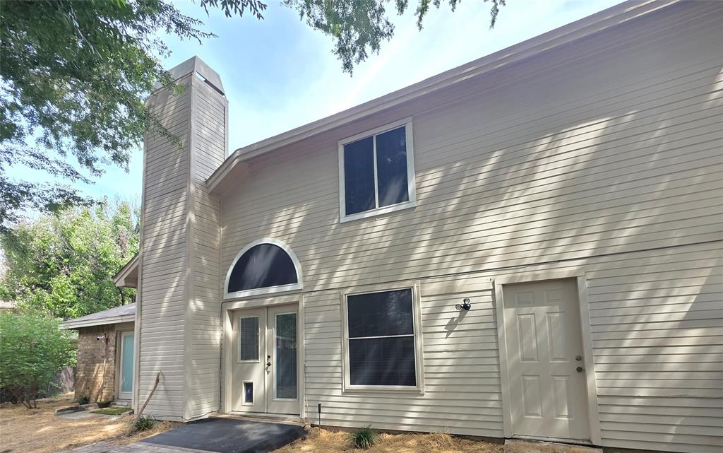 Exterior facade featuring horizontal siding, a prominent chimney, an arched window, and double entry doors
