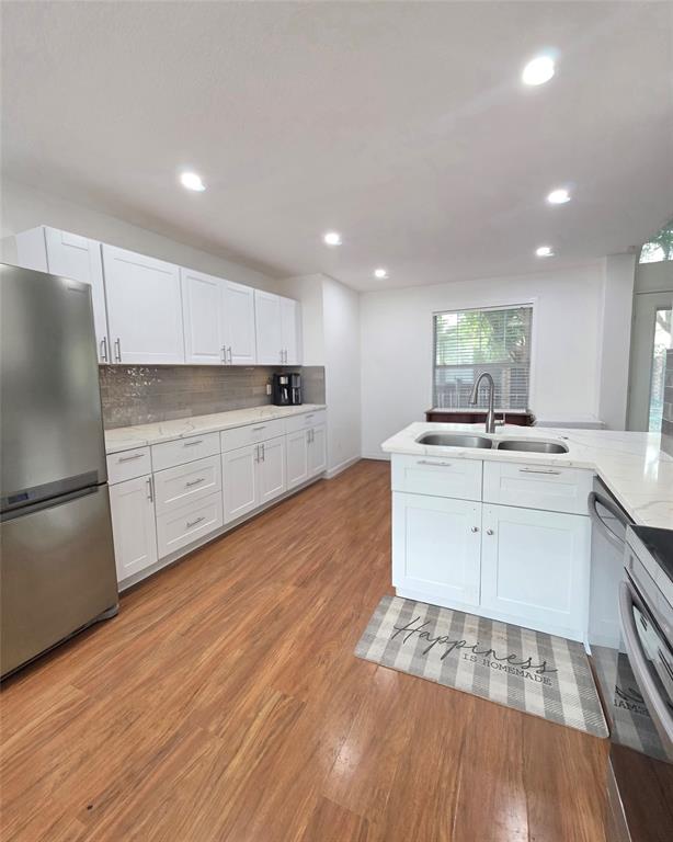 Kitchen featuring white shaker-style cabinetry, quartz countertops, a stone-finish tile backsplash, stainless steel appliances, and wood-finish flooring