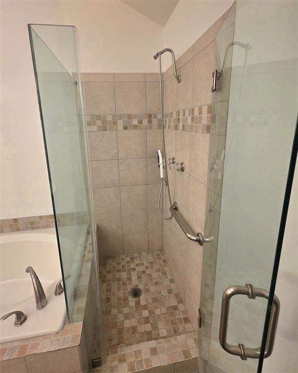 Walk-in shower featuring a glass enclosure, wall-mounted showerhead, tiled surround with a decorative mosaic accent, and a built-in metal grab bar, accompanied by a soaking tub with deck-mounted fixtures