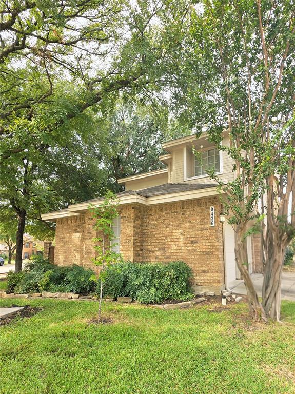 Two-story exterior featuring multi-material brick and siding facade, manicured lawn, and established trees