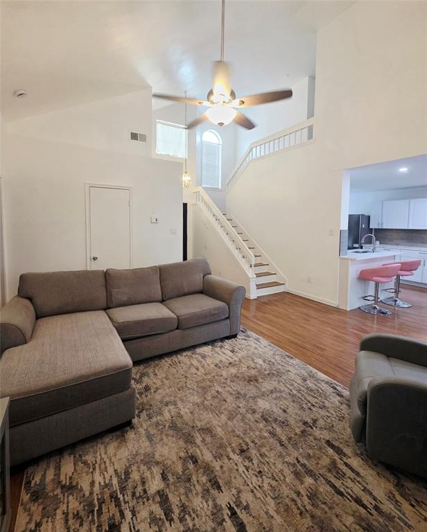 Vaulted ceilings, staircase with white railing, wood-finish flooring, arched window, and overhead ceiling fan