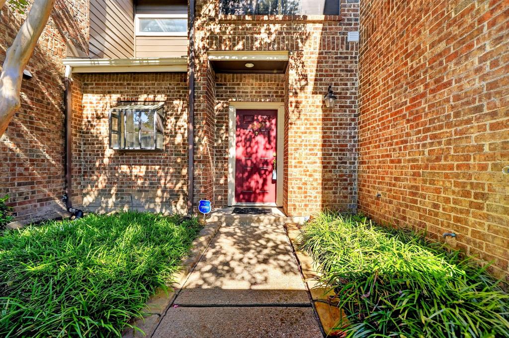 Exterior entrance featuring a full-brick facade, a concrete walkway, a solid-color front door, and established ground-cover landscaping