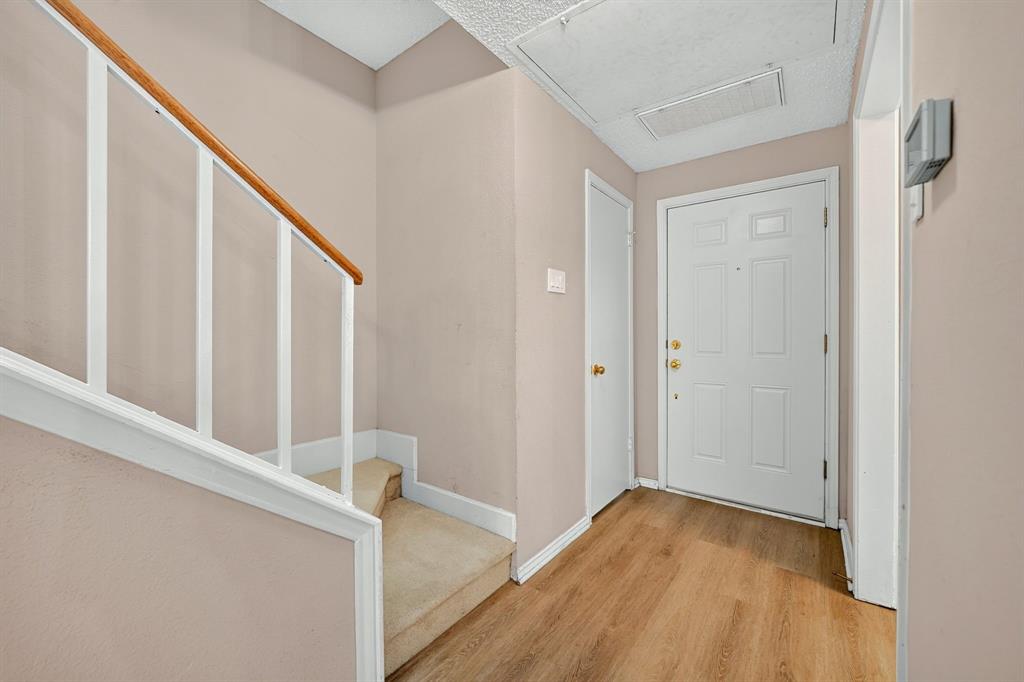 Entryway featuring wood-finish flooring, a solid-core six-panel door with gold-tone hardware, and a staircase with a white-finished railing and wood-tone handrail