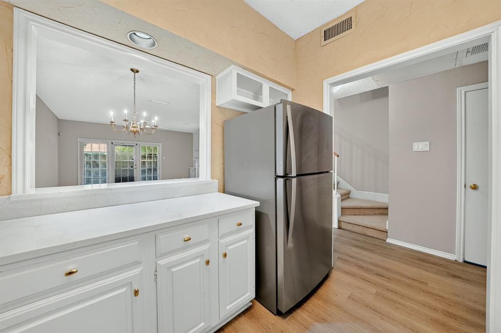 White cabinetry with stone-finish countertops, stainless steel refrigerator, and wood-finish flooring