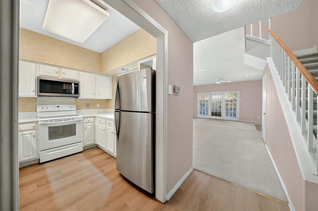 Kitchen featuring white cabinetry, wood-finish flooring, and stainless steel appliances, paired with an interior staircase boasting a white handrail and wooden banister