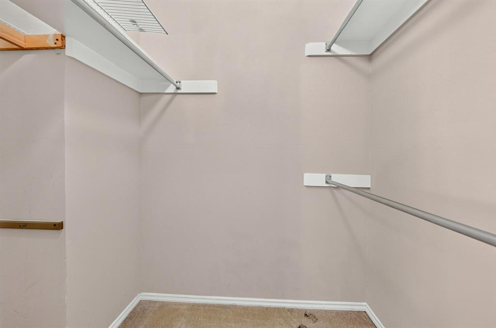 Walk-in closet featuring white wall-mounted shelving and integrated metal hanging rods