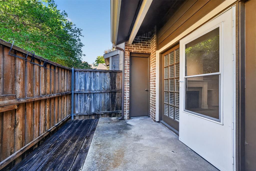 Private outdoor patio featuring a concrete slab, wood-plank flooring, brick exterior masonry, and a wood privacy fence