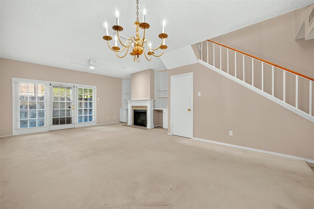 Fireplace with detailed mantel, built-in shelving, glass-paned sliding doors, tiered chandelier, and staircase with wooden handrail