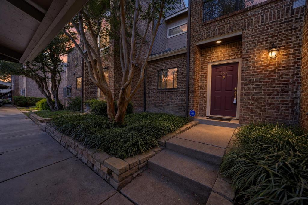 Brick exterior featuring a recessed entry, concrete walkway, retaining walls with tiered landscaping, and wall-mounted exterior lighting