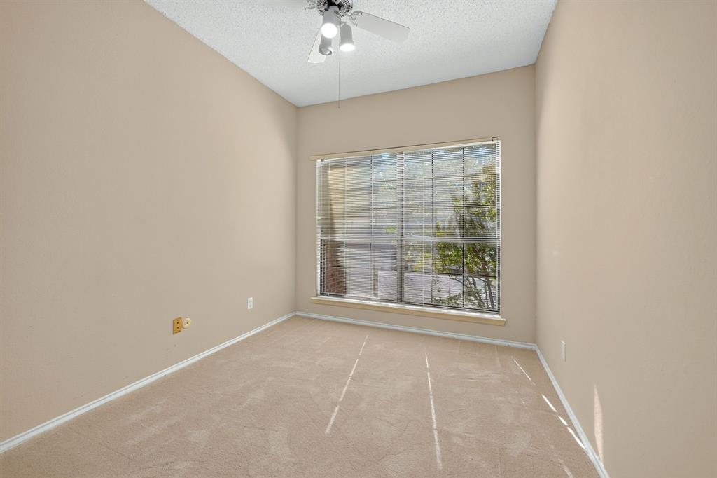 Neutral-toned interior space featuring neutral carpeting, a large grid-pattern window, and a ceiling-mounted light fixture with a fan
