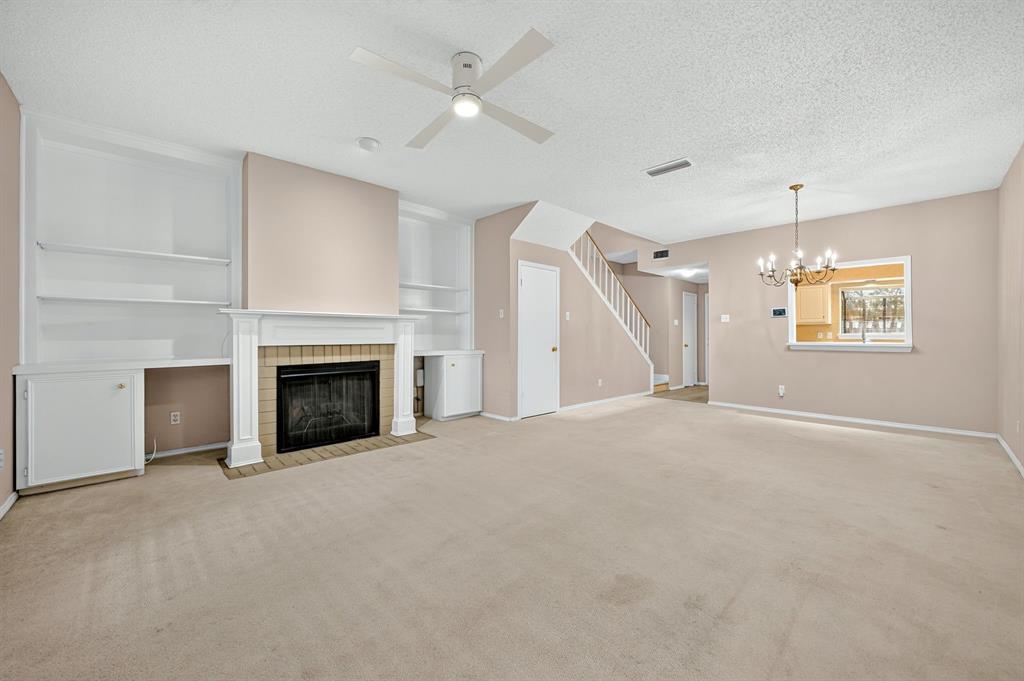 Fireplace with tiled surround, built-in shelving, ceiling fan, and chandelier fixture