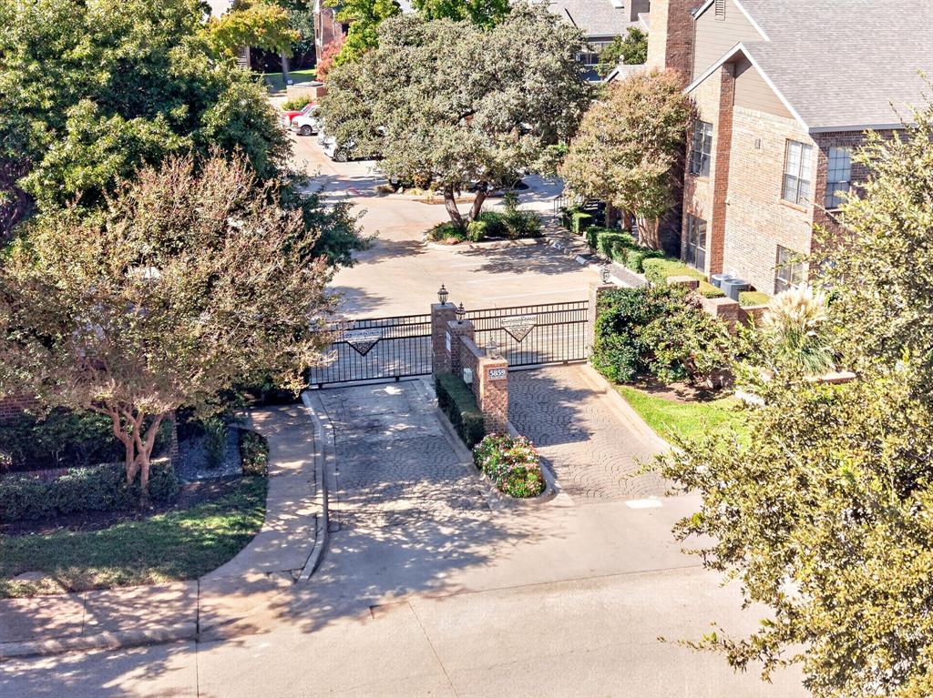 Gated entrance featuring decorative iron fencing, brick-pillar accents, stone-paver driveway, and mature landscaping