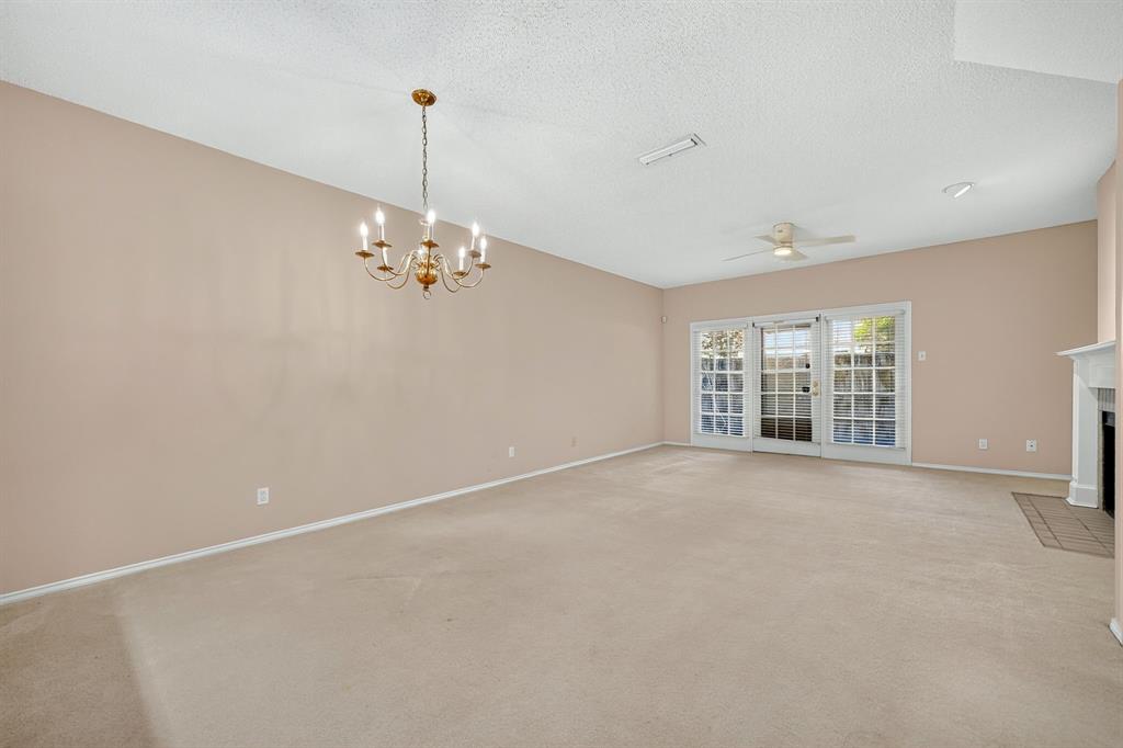 Open living area featuring a traditional multi-arm chandelier, ceiling fan, fireplace with a mantle, and glass-paned French doors