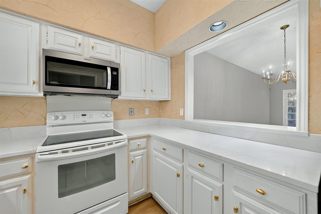 Kitchen featuring white cabinetry with gold-tone hardware, stone-finish countertops, and stainless steel microwave