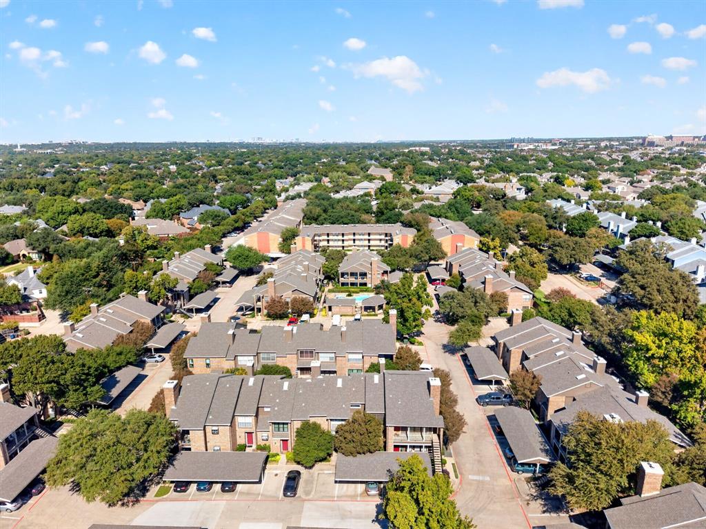 Aerial perspective of a multi-unit complex featuring shingled roofs, brick and masonry siding, covered parking structures, and mature landscaping