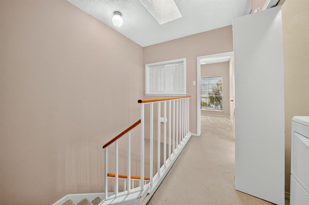 Staircase featuring a white metal railing with a wood-finish handrail, window with plantation-style shutters, and flush-mount ceiling lighting