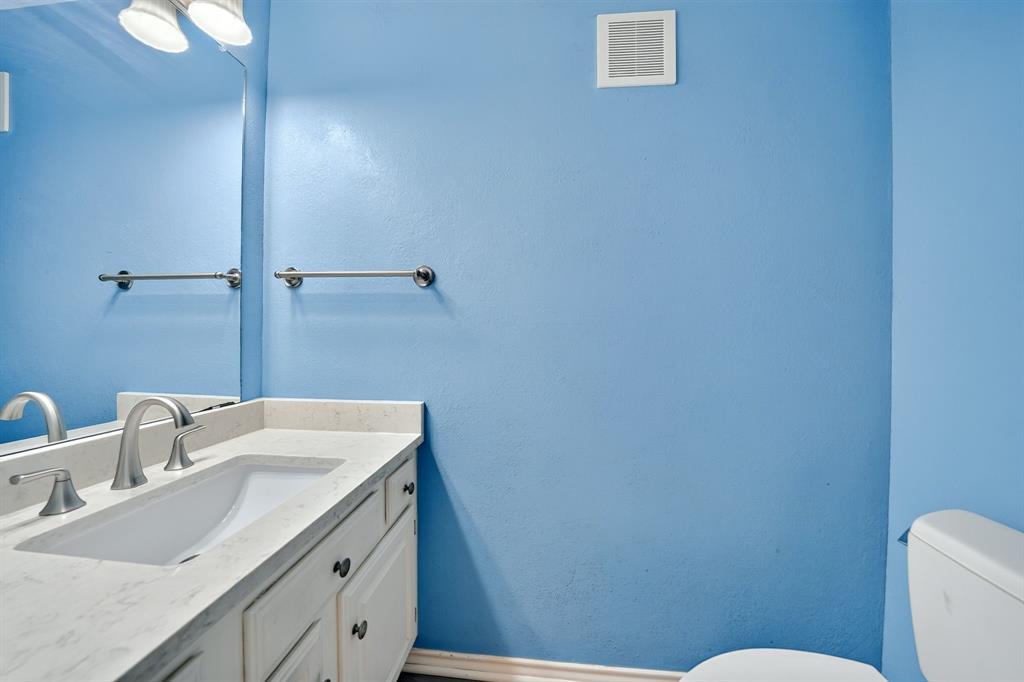 Bathroom featuring a vanity with a stone countertop, an integrated rectangular sink, a polished metal faucet, a full-width wall mirror, and dual light fixtures