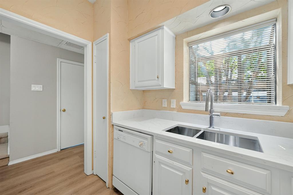 Kitchen featuring white cabinetry, solid-surface countertops, dual-basin stainless steel sink with high-arc faucet, integrated dishwasher, and wood-finish flooring