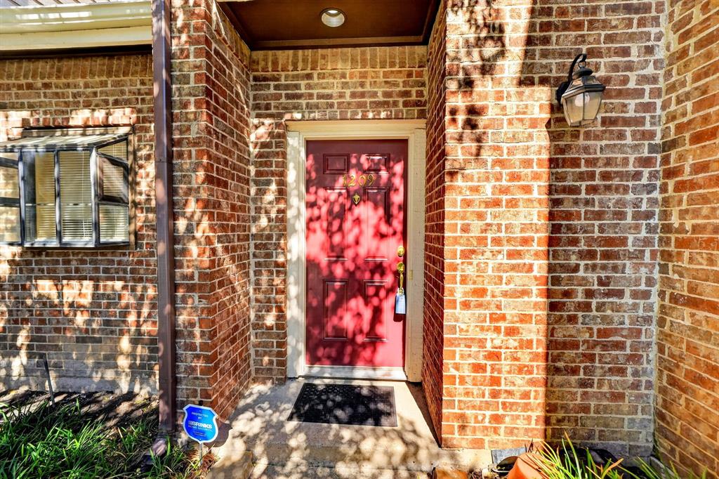 Exterior entrance featuring full-height brick masonry, a paneled door with brass-finish hardware, and a wall-mounted lantern-style fixture