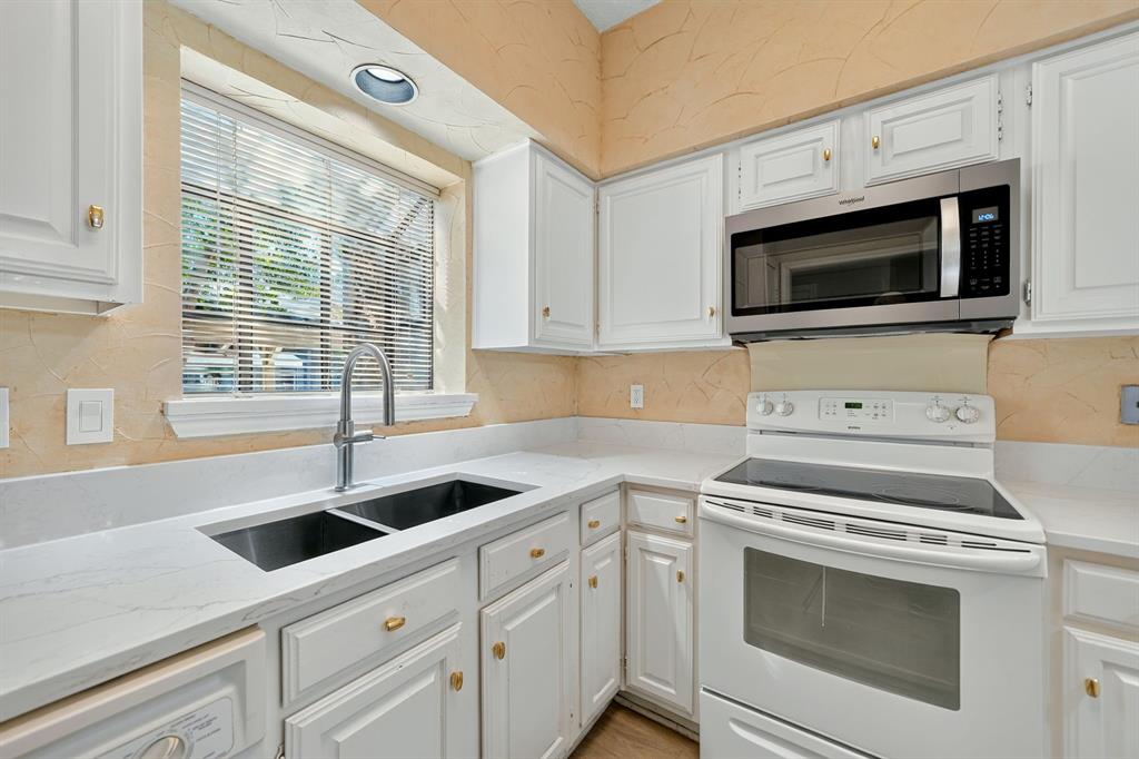 Kitchen featuring white shaker-style cabinetry, quartz countertops, dual-basin undermount sink with high-arc faucet, and stainless steel over-the-range microwave