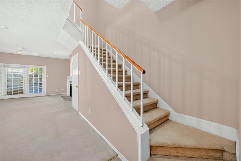 Staircase with white railing and wood-tone handrail, carpeted steps, glass-paneled exterior door, and fireplace surround