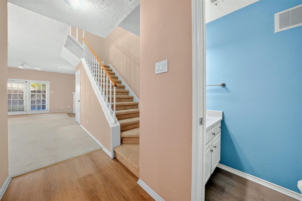 Staircase with white railing and wood-finish handrail, carpeted steps, wood-finish flooring, white vanity with stone-top surface, and dual French doors