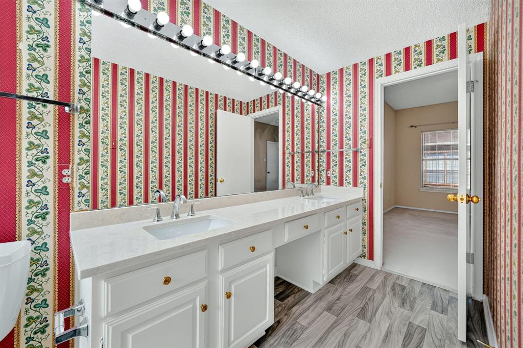 Bathroom vanity featuring a light-toned countertop, dual integrated sinks, white cabinetry, a full-width wall mirror, and wood-finish flooring
