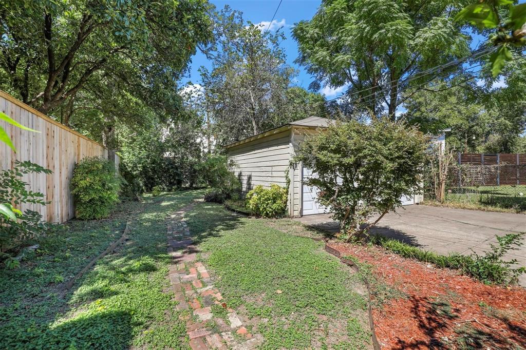 Rear exterior featuring a detached garage, concrete driveway, brick pathway, wood privacy fencing, and mature trees