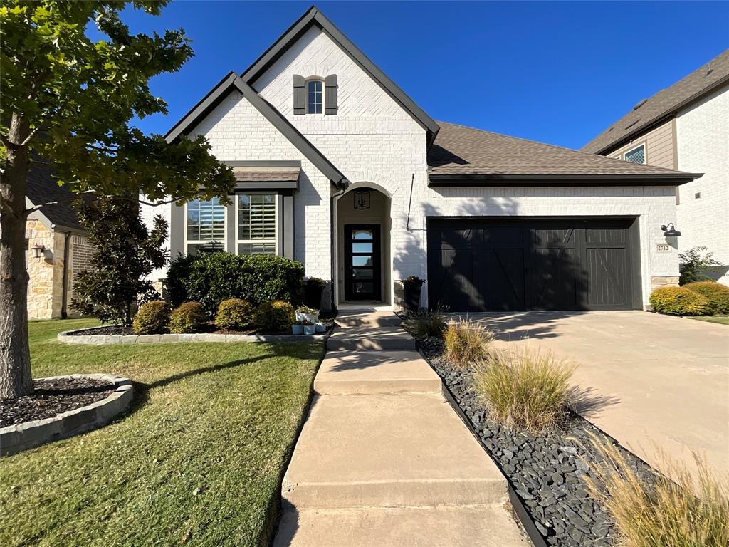Painted brick exterior with a steep-pitched gable roof, dark-finished garage door with decorative cross-bracing, covered arched entryway, and concrete walkway