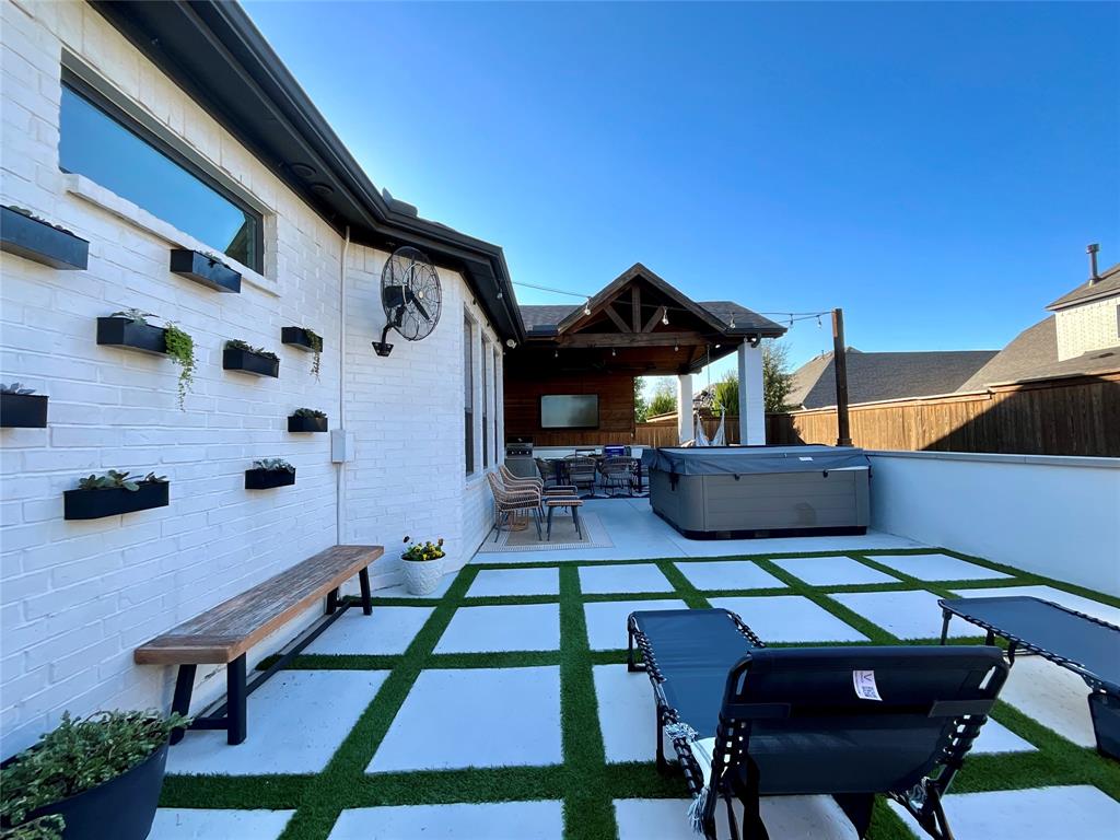 Patio area featuring a painted brick exterior, wall-mounted planters, geometric concrete pavers with grass inlay, and a covered timber-framed structure