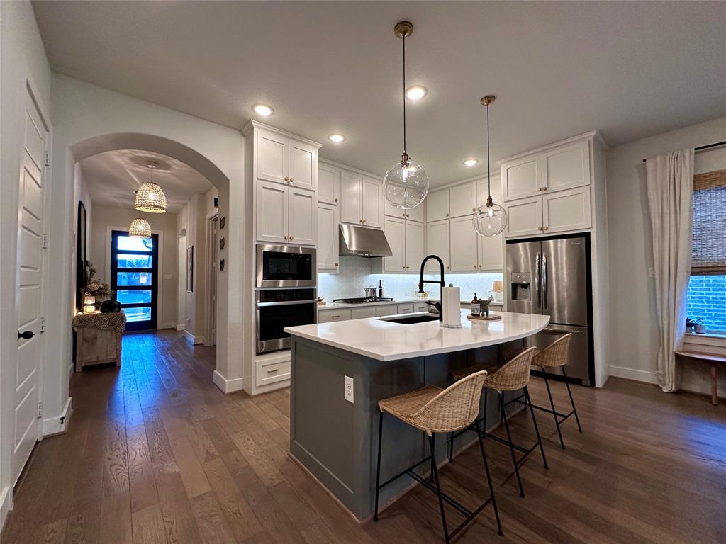 Kitchen featuring white ceiling-height cabinetry, quartz countertops, a contrasting central island, stainless steel built-in appliances, and wood-finish flooring