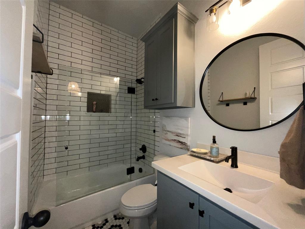 Bathroom featuring subway tile shower surround, glass enclosure, slate-colored cabinetry, solid-surface vanity countertop, and matte black fixtures