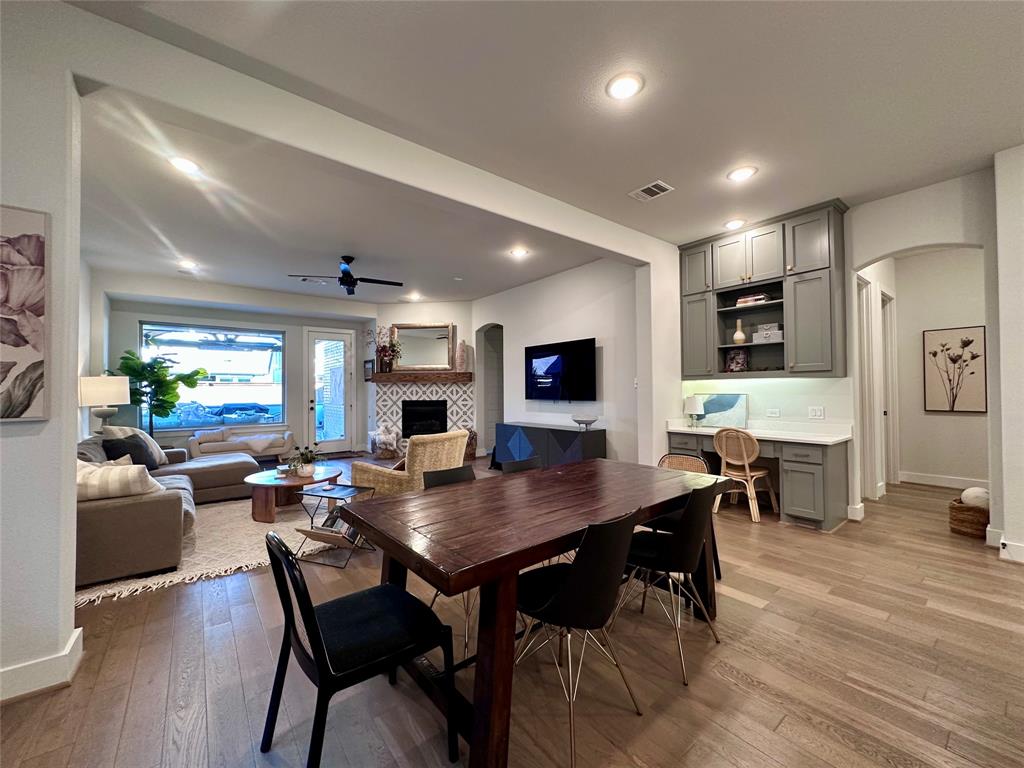 Open-concept interior featuring wood-finish flooring, recessed lighting, a built-in office workstation with overhead cabinetry, and a fireplace with a patterned tile surround and a wood mantel
