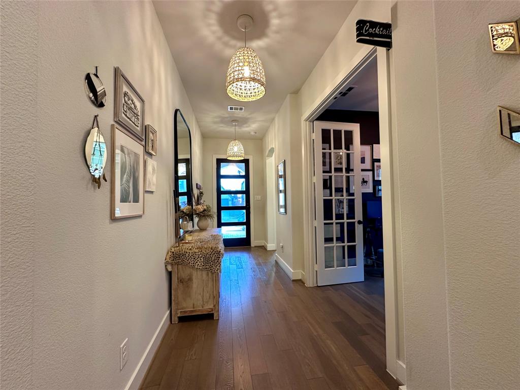 Entryway featuring wood-finish flooring, dual woven pendant light fixtures, and a glass-paneled front door with horizontal grid detailing, complemented by a multi-pane French door